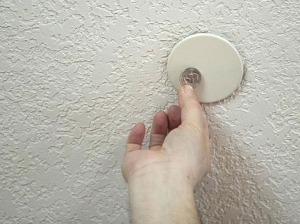 A quarter held next to a ceiling sprinkler cover plate for scale; the plate's diameter is 5-6 times larger