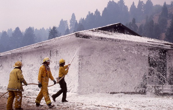 Firefighters apply foam to a building's exterior with specialized spray nozzles