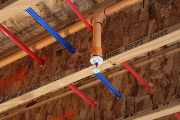 A fire sprinkler mounted on orange synthetic pipe in unfinished construction