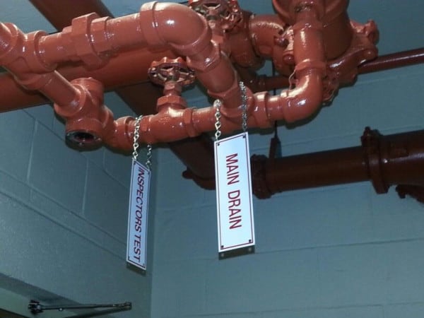 Signs for main drain and inspectors test valves hanging from fire sprinkler pipes