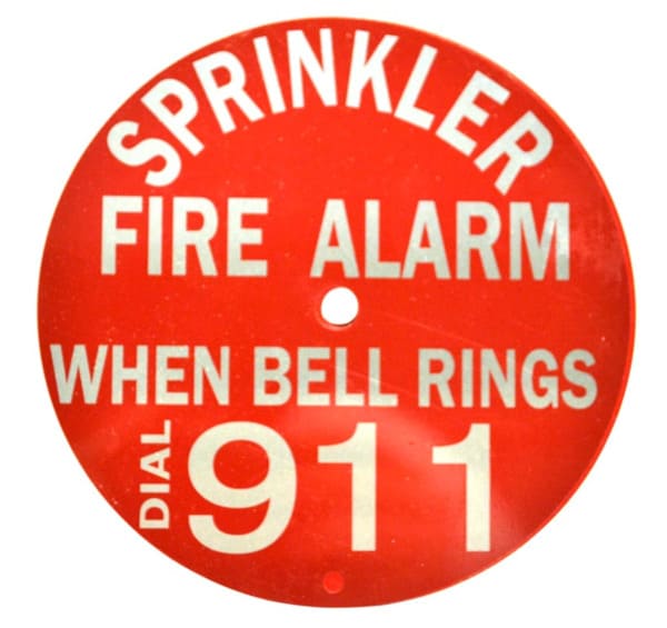 Round sign reading "sprinkler fire alarm when bell rings dial 911"