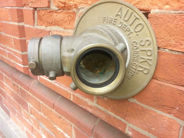 An exposed brass fire department connection with clogged inlets