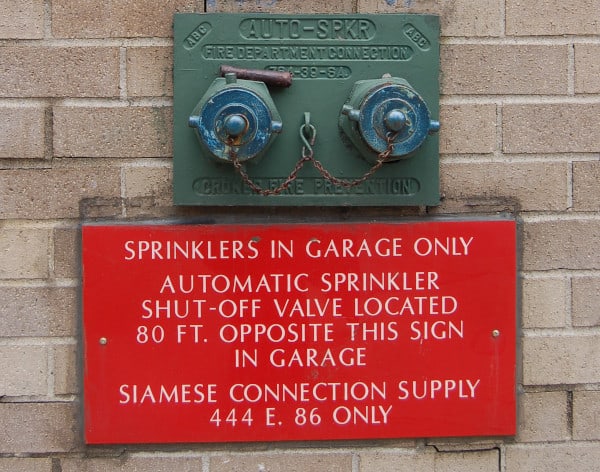 A flush fire department connection with sign reading "sprinklers in garage only"