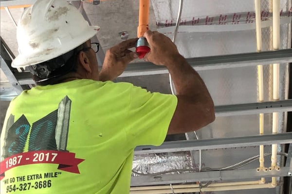 An employee of a fire sprinkler contractor installs a sprinkler head